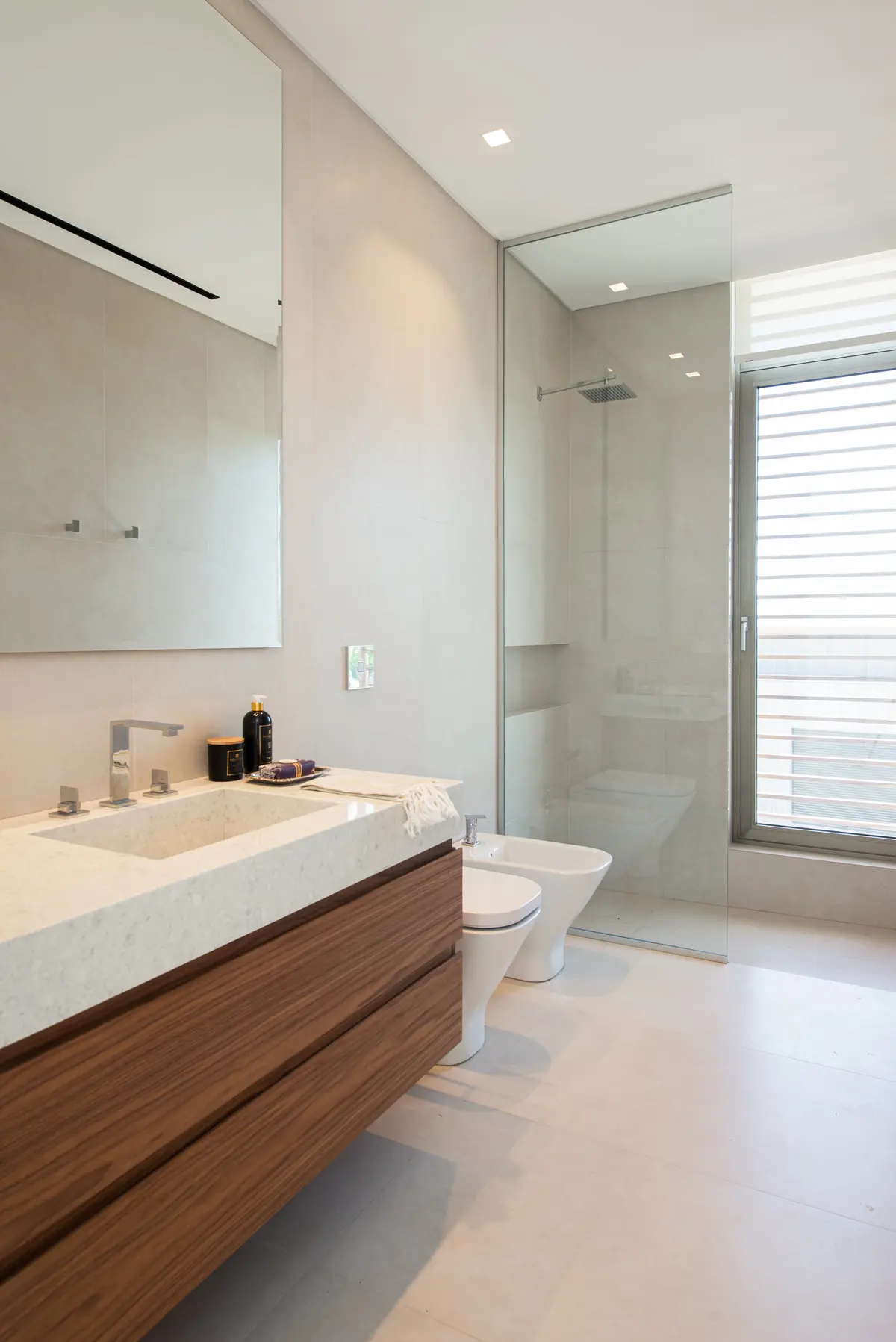 Baño moderno con vanitory flotante de madera oscura y bidet — proyecto Casa AA, por Estudio Junor, en Pilar
